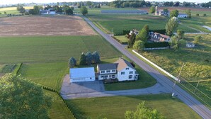 Vista aerea di una grande casa bianca con un'ampia strada privata e campi adiacenti.