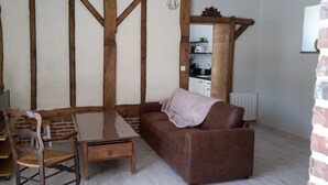A cozy living room with a brown sofa, a wooden dining table, and a brick wall. - Comfortable farm cottage 10 minutes from the sea (Bosville)