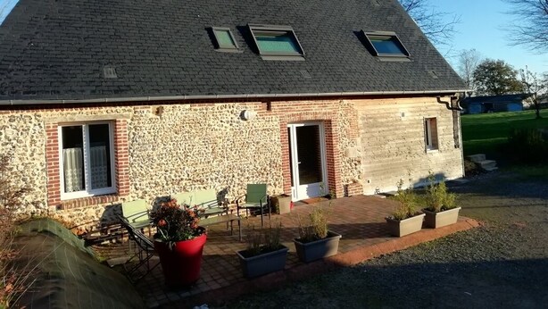 A stone building with a sloped roof, two windows, a door, and a small patio area with chairs and potted plants. - Comfortable farm cottage 10 minutes from the sea (Bosville)