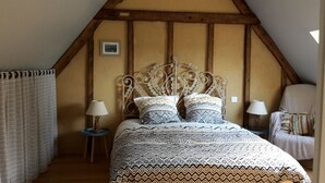A bedroom with a sloped ceiling, a bed with patterned bedding, two bedside lamps, a small table, and a chair. - Comfortable farm cottage 10 minutes from the sea (Bosville)