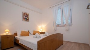A bedroom with a wooden bed, two bedside tables with lamps, a window with curtains, and a small painting on the wall.
