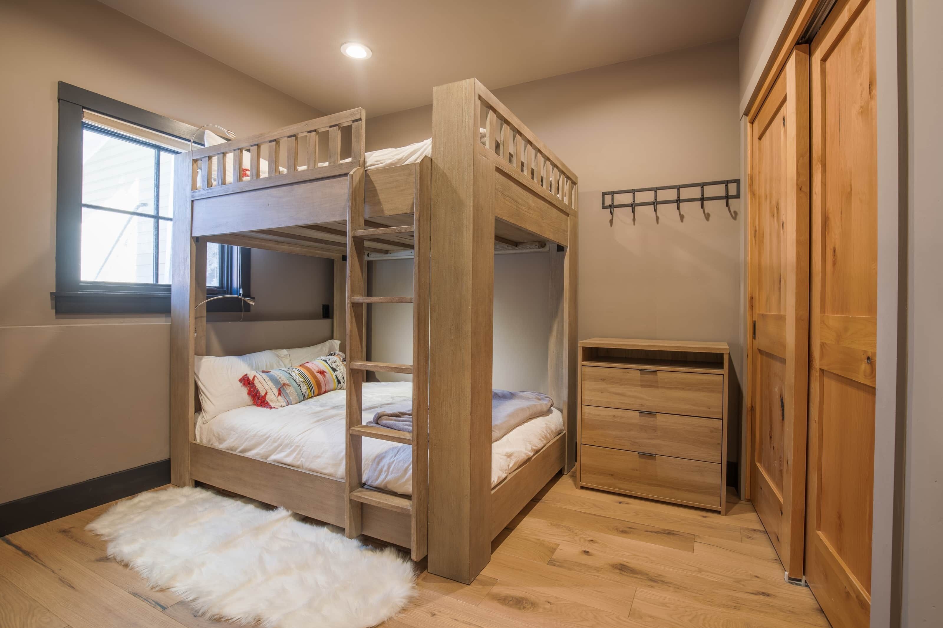 A bunk bed room with a wooden wardrobe and a small desk.
