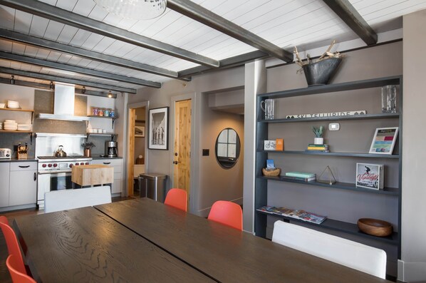 A modern kitchen with white cabinets, a wooden table, and orange chairs. There is a bookshelf with various items and a framed picture on the wall. - Slopestyle: Steps to Mountains & Main Street (Telluride)