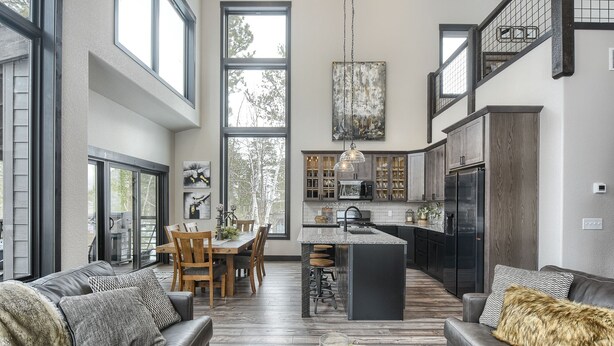 Amplia sala de estar con un ventanal grande, comedor y cocina con alacenas de madera oscura y un refrigerador negro.