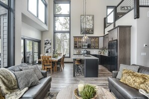 Amplia sala de estar con un ventanal grande, comedor y cocina con alacenas de madera oscura y un refrigerador negro.