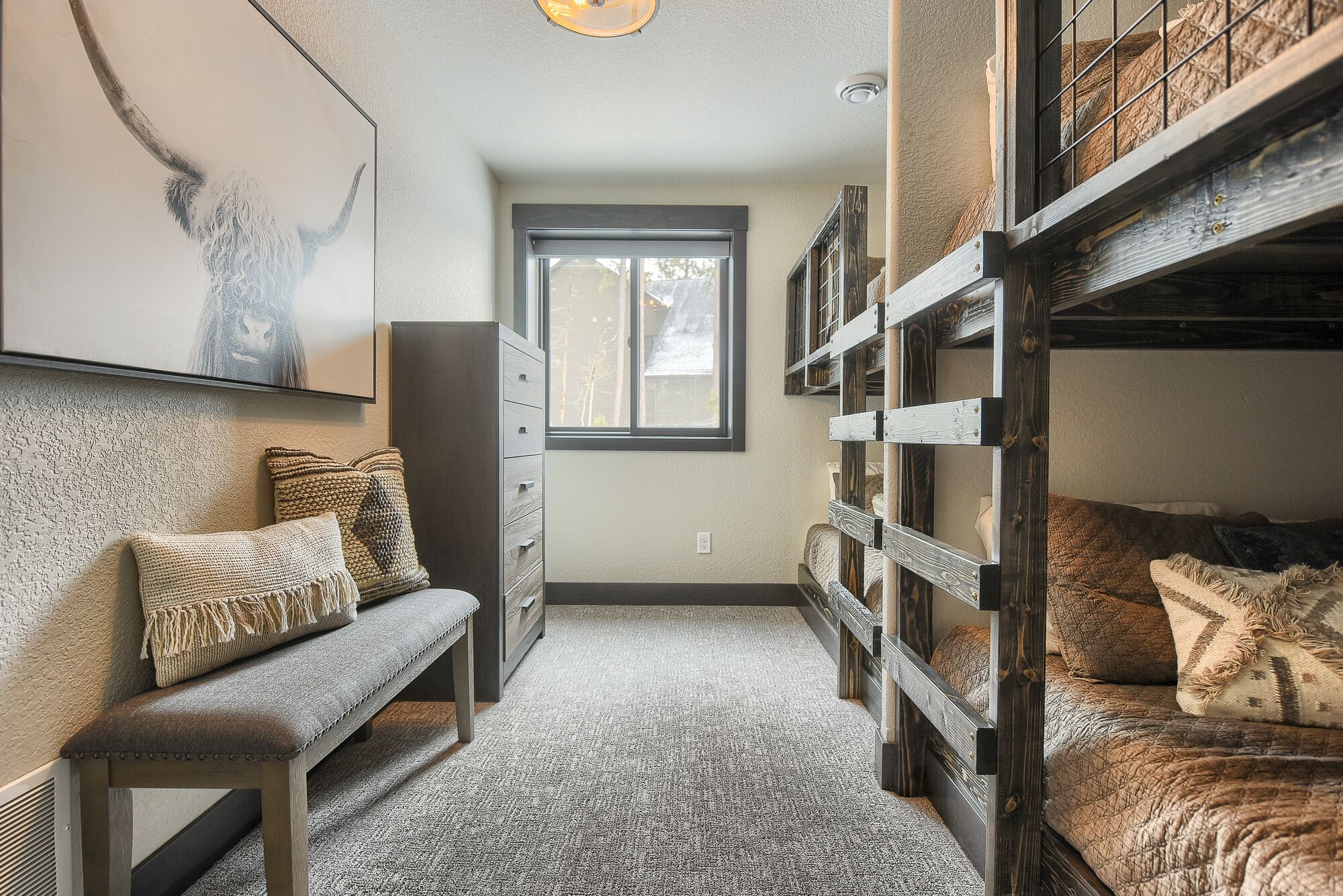 A cozy bedroom with a bunk bed, a bench, a dresser, and a window.