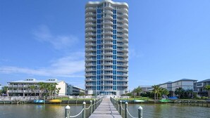 Un hotel alto y moderno con una fachada curva, situado cerca de una ribera con un muelle que da al agua.