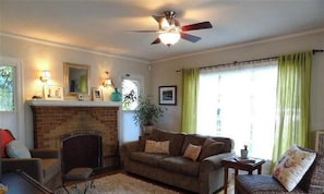 A living room with a fireplace, a ceiling fan, a sofa, and a window with curtains.