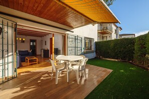 En terrasse med et træbord og stole, en sofa, og et overdækket område med et gult markise.