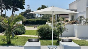 A modern outdoor seating area with two white cushioned benches, a white umbrella, and a pool reflecting the surroundings. - LM7 VILLA a stone's throw from the sea, Infinity Pool, Hydro, Wi-Fi, Garden (Fontane Bianche)