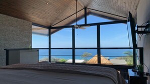 Une chambre avec un grand lit, un plafond en bois et une vue sur l’océan.