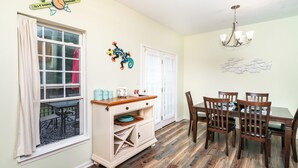 A dining area with a wooden table and chairs, a white cabinet with shelves, a window with curtains, and a wall-mounted decoration. - Seaclusion Near Bethany Beach (Ocean View)