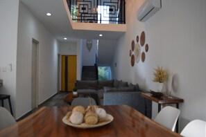 A modern dining area with a wooden table, a plate of pastries, and a staircase leading to a balcony. - Hola, Paradise/Pool, Gym, & Tropical Escape (Puerto Morelos)