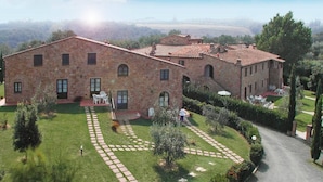Un edificio in pietra con tetto in tegole rosse, un giardino pavimentato con un sentiero sinuoso e un'area salotto all'aperto.