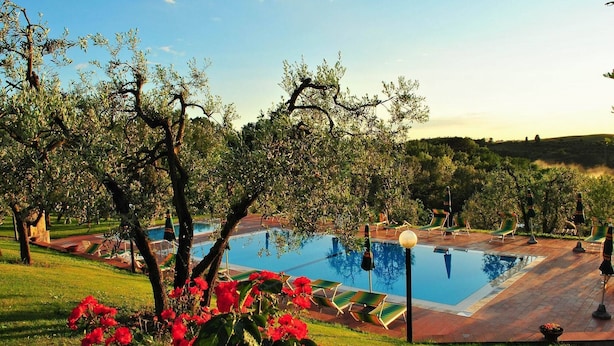 Una piscina circondata da alberi e prato, con lettini e un cielo sereno.