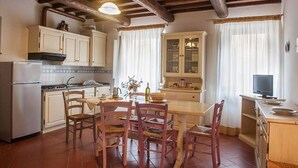 Una cucina con travi in legno, un tavolo da pranzo con sedie, un frigorifero e un televisore su un mobile.