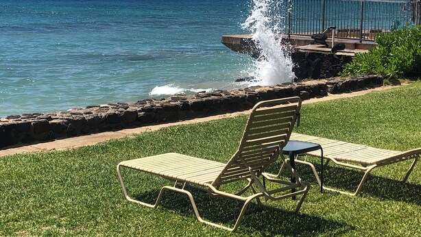 Une zone herbeuse avec deux chaises longues donnant sur une côte rocheuse et une étendue d’eau.