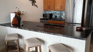 Une cuisine moderne avec des meubles en bois, un réfrigérateur en acier inoxydable, un four à micro-ondes et un grand îlot central doté de tabourets de bar.