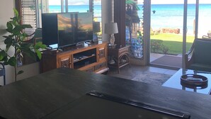 Un salon équipé d’un téléviseur, d’un meuble de rangement en bois et offrant une vue sur l’océan grâce à de grandes portes-fenêtres coulissantes.