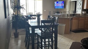 A dining area with a table and chairs, a ceiling fan, and a television displaying a sports game.