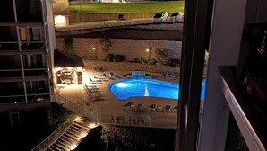 A nighttime view of a hotel with a swimming pool, lounge chairs, and a well-lit outdoor area.