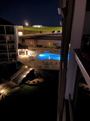Une vue nocturne d'un hôtel avec une piscine, des chaises longues et un espace extérieur bien éclairé.