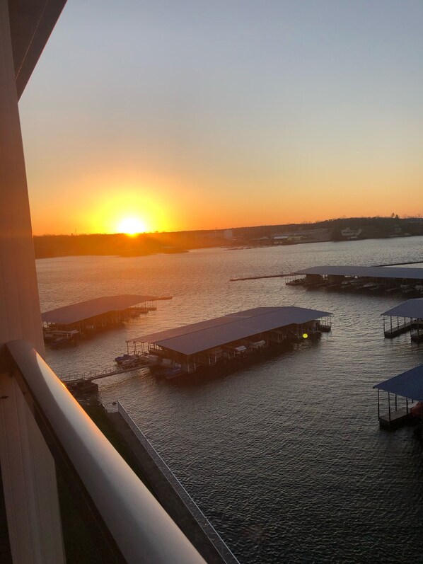 A sunset view from a balcony overlooking a marina with several docked boats and covered structures.