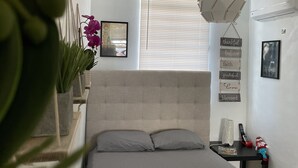 Un dormitorio con cama, mesita de noche, aire acondicionado instalado en la pared, ventana con persianas y ventilador de techo.