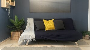 Una sala de estar moderna con una pared azul oscuro, un cuadro abstracto de gran tamaño, un sofá azul oscuro con cojines amarillos y negros, una manta blanca y tres estanterías de madera con plantas.