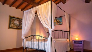 Una cama con dosel, ropa de cama blanca, una mesita de noche con lámpara y dos cuadros enmarcados en la pared.