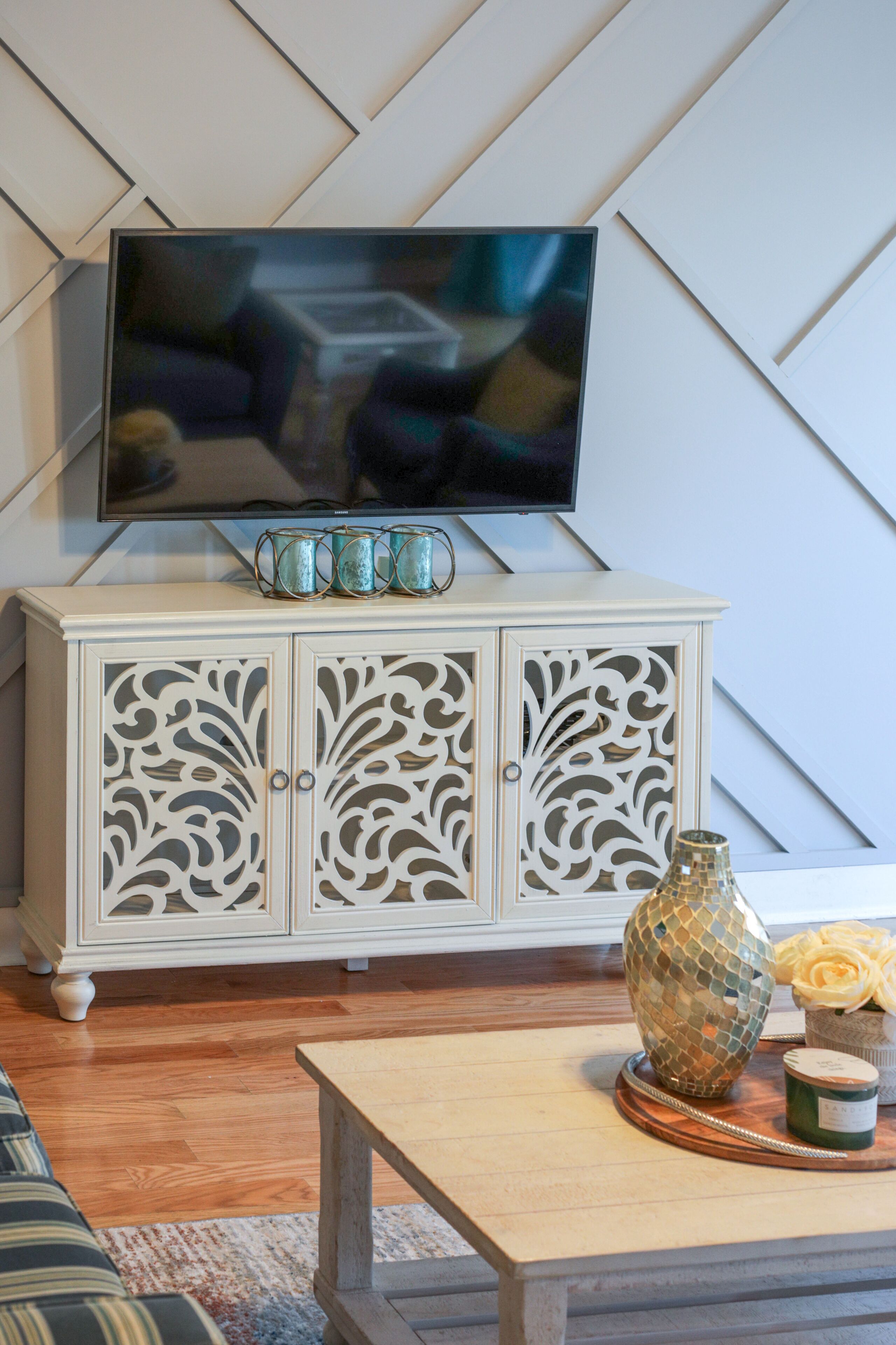 A living room with a flat-screen TV mounted on a white cabinet with intricate cut-out designs.