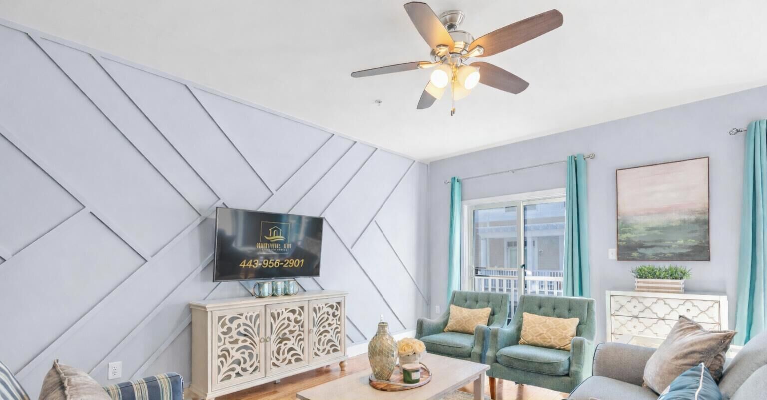 Un salon moderne avec un ventilateur de plafond, un téléviseur fixé au mur et une fenêtre avec des rideaux.