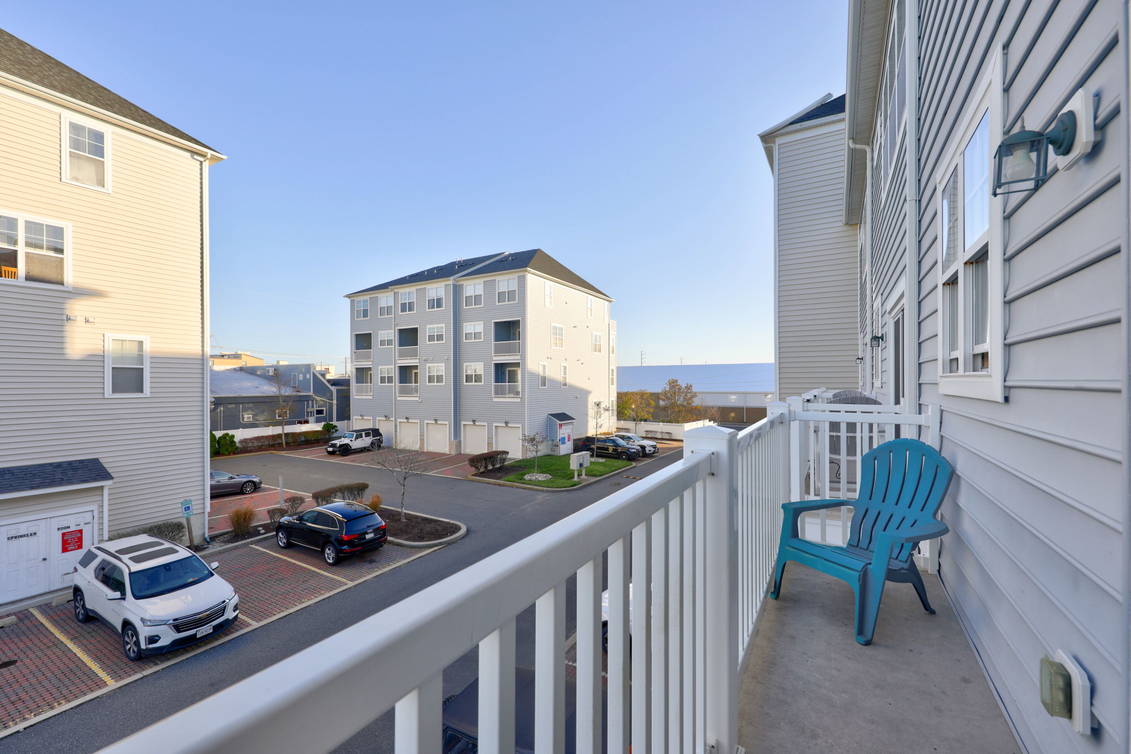 A residential building with a balcony, a blue chair, and parked cars.