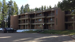 Un immeuble en bois à plusieurs étages, doté de balcons, d’un espace de stationnement et d’un sol recouvert de neige.