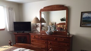 Une chambre à coucher avec un lit, une commode en bois, un téléviseur et un miroir.