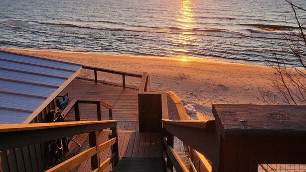 Una escalera de madera que lleva a una playa con un atardecer de fondo.