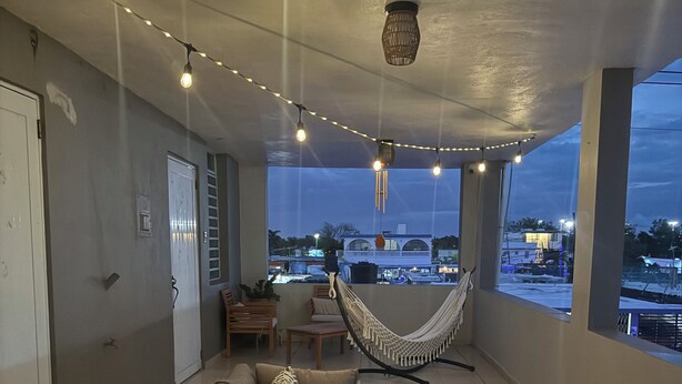 Un espacio al aire libre acogedor con una hamaca, sofás acolchados e iluminado con guirnaldas de luces.