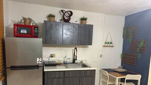 Cocina compacta con refrigerador, microondas y un pequeño comedor con mesa y sillas.