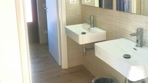 A bathroom with two sinks, a mirror, and a trash bin.