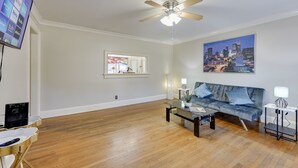 A modern living room with a flat-screen TV, a ceiling fan, a cityscape painting, a sofa, and a coffee table. - Atlanta Luxury Home 1 mi from The Battery Sleeps 8 (Smyrna)