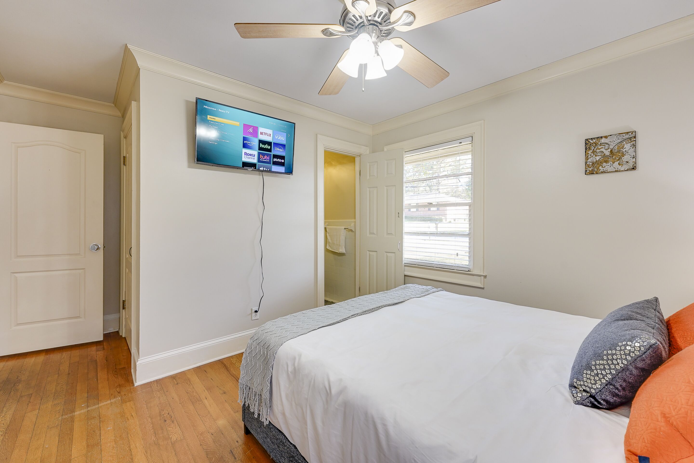A bedroom with a bed, a ceiling fan, a TV mounted on the wall, and a window.