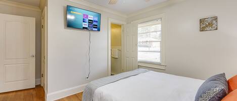 A bedroom with a bed, a ceiling fan, a TV mounted on the wall, and a window.