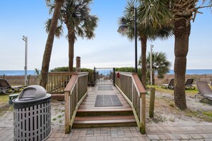 Walk along the beachside boardwalk, flanked by palm trees, to a relaxing deck area with lounge chairs.