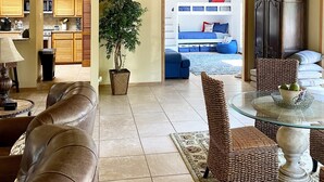 A spacious living area with a leather sofa, a glass coffee table, wicker chairs, a dining table, and a ceiling fan.