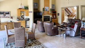 A spacious living room with a fireplace, a dining area with wicker chairs, a kitchen with wooden cabinets, and a staircase leading to another level.