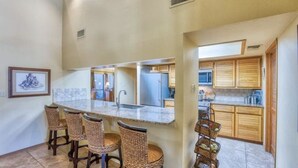 A kitchen with a central island, bar stools, wooden cabinets, and a microwave.