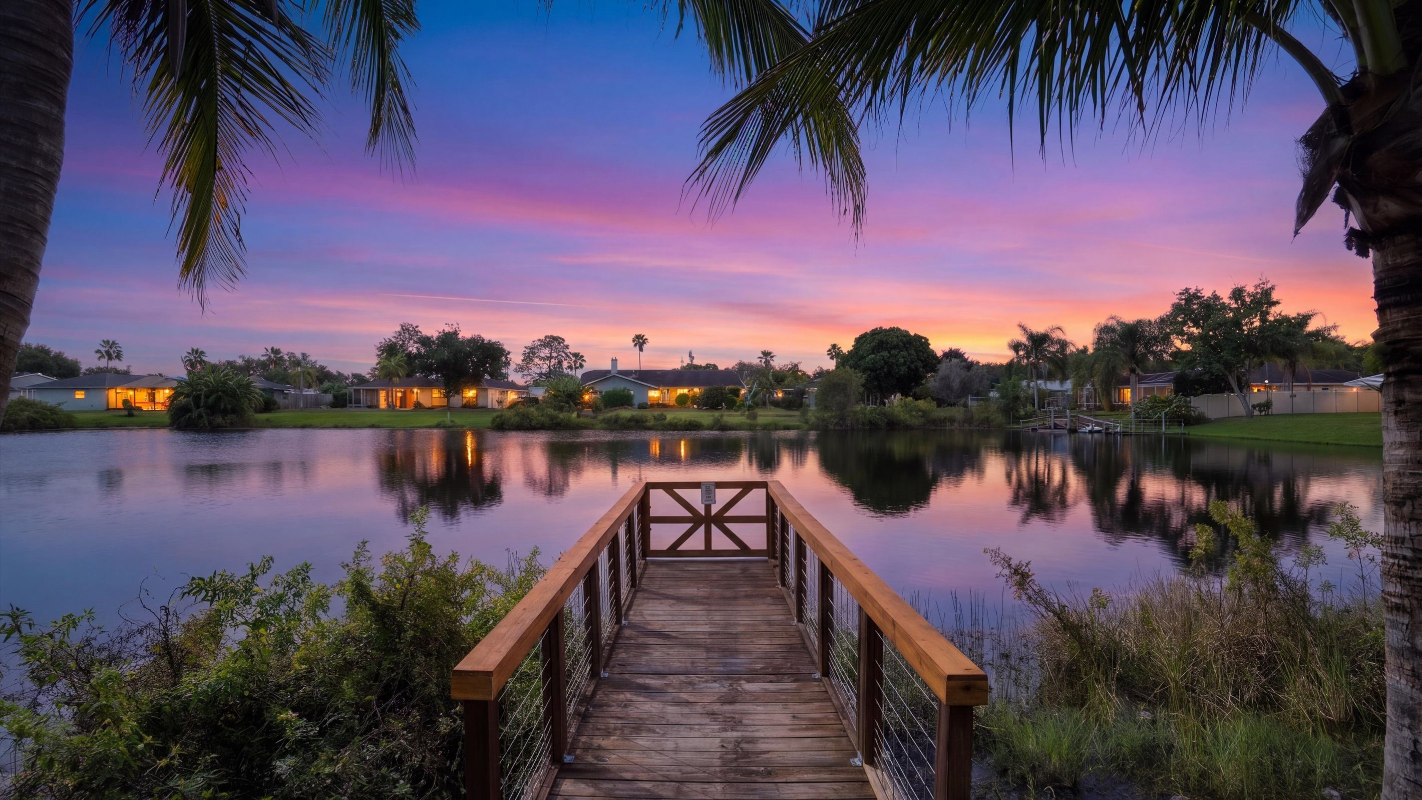 Um cais de madeira leva a um lago calmo, com um pôr do sol ao fundo.