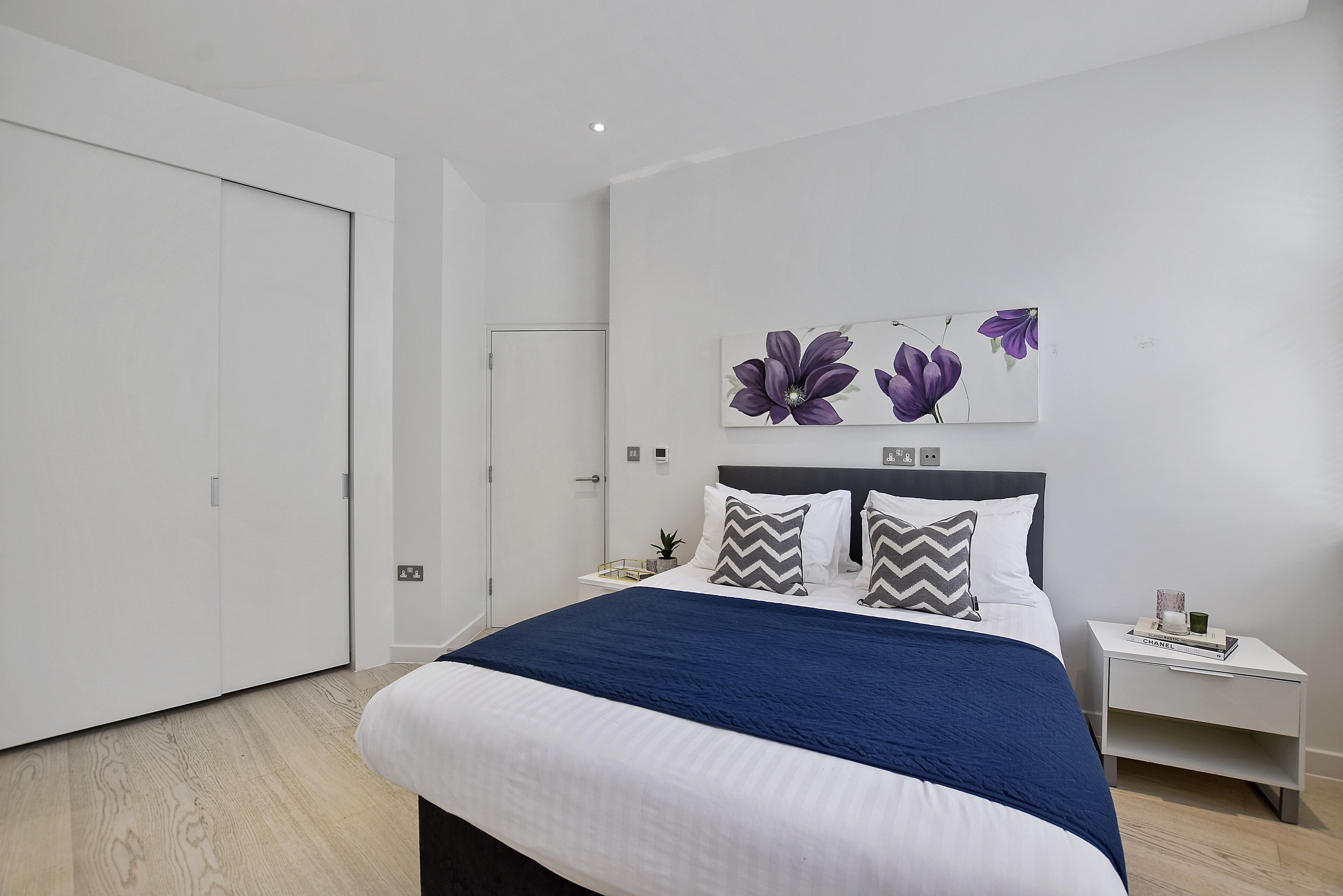 A modern bedroom with a large bed, a nightstand, and a wall-mounted artwork.
