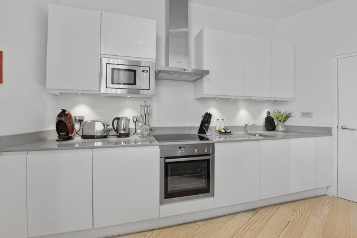 Una cocina moderna con armarios blancos, un microondas de acero inoxidable, una tetera y una cafetera.