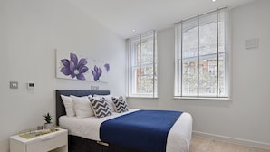 A modern bedroom with a bed, bedside table, and a window with blinds.